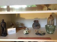 Shelf containing John Letts sculpture, Wartook pottery vase, Devon creamer, and green glass bowl arranged with a ruler showing scale