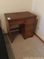 Front angle view of wooden single pedestal desk with drawer on left and three drawers on right, placed against wall.