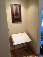 Adjustable tilt drawing table and framed print hanging on wall above it in a corner of a room.