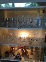 Full cabinet view showing all glassware, carafe, copper goblets, and salt and pepper set on shelves under cabinet lights.