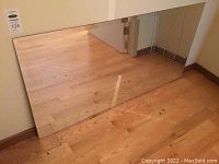 Full view of the large rectangular unframed beveled mirror resting against a wall on wood floor.