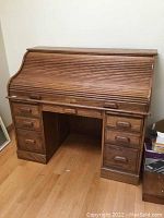 Closed roll-top desk showing smooth curved tambour wooden cover and multiple drawers on either side.