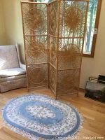 Wide shot of the three-panel wicker screen and oval rug in a room beside a chair and window