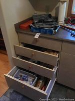 Photo showing open drawers and countertop with multiple hand tools, tool boxes, and tool sets.