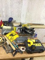 Full table view showing assortment of tools and supplies including Dewalt drill, socket set, heat tool, jigsaw, wood block file, chalk line, paint roller, and brushes.