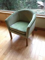 Green tub chair angled side view showing upholstery and wooden legs.