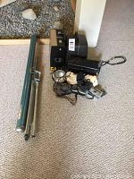 Overview of vintage projector, cameras, tripod stand, and screen components on carpeted floor.