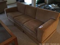 Front-facing view of vintage three-seat sofa in a brown/tan fabric with three cushions and angled arms.