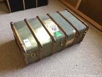 Photo of the top and side angles of the vintage trunk showing the wood strip reinforcements, metal hardware, and aged travel labels.