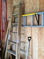 Wooden 7-step ladder leaning against plywood wall with some other tools hanging nearby.