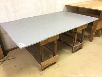 Front angled view of saw horse style work bench with grey surface top and wooden saw horse base