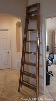 Full view of the 8 ft wooden ladder standing upright indoors showing steps and overall condition.