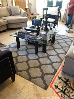 View of the area rug placed on tile flooring under a glass coffee table and between furniture in a living room setting.