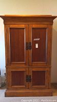 Front view of the wooden armoire showing the two upper cabinet doors with dark metal handles and the overall finish.