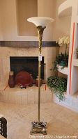 Full view of tall brass floor lamp standing next to a fireplace, showing the white glass globe shade and brass stem with leaf decoration.