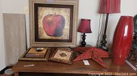 Photo showing two lamps, a large red vase, three metal stars in different sizes, and four framed pictures arranged on a wooden surface.