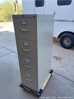 Full front angle view of the tall, beige metal filing cabinet showing four drawers and handles, standing on a dolly.