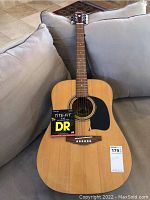 Full view of the guitar showing natural wood finish and black pickguard with attached box of DR Tite-Fit strings.