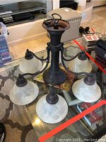 Full view of metal chandelier with six glass bell-shaped frosted shades on a round table.