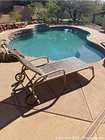 Poolside lounge recliner featuring an aluminum frame, positioned beside a pool on a concrete surface.