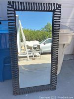 Front view of the large rectangular mirror showing the reflective surface and the full metal frame with cut-out wave pattern design.