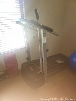 Gray Pro-Form treadmill with folded upright design next to window, visible power cord and base with resistance bands.