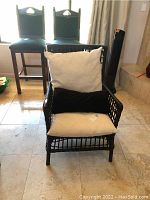 Front view of the black wicker chair with cream seat pillow, cream back pillow, and black lumbar throw pillow, showing chair structure and cushions.