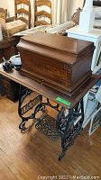Full view of antique sewing machine cabinet with wooden top closed, showing dark wood grain and cast iron base with 'HOUSEHOLD' nameplate.