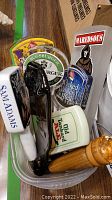 Beer tap handles including Sam Adams, black wooden handle, Augsburger Beer, Old Tankard Ale, and others in plastic bin.