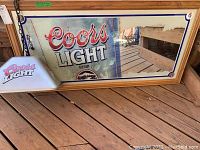Coors Light mirror with prominent branding and reflective surface in wooden frame.