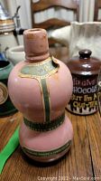 Pink ceramic decanter with Portuguese label and metal rim, detailed close-up showing wear and patina.
