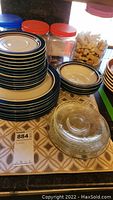 Stack of multiple Carousel stoneware plates in beige and blue, glass dishes with lids in front, and jars in background