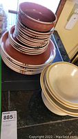 Stacked Hearthside Garden Festival stoneware plates and bowls with glazed brown interior and colorful edge pattern, plus a set of off-white Dansk Mesa stackable bowls.