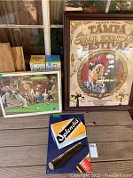Framed signed Tampa Cigar Heritage Festival poster, dog playing pool print, and cigar ad metal sign shown together.