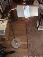 Full view of chrome adjustable floor lamp standing upright, showing circular base, adjustable arm, and rectangular shade.