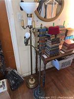 Photo of two metal base floor lamps next to a wall and table with books, showing full view of lamps.