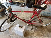 Red Schwinn X-tra Lite Traveler men's road bike with drop handlebars, black saddle, pedals with toe clips, and extra bike parts on a white box.