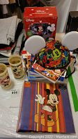 Photo of colorful Mickey Mouse ear hat, boxed Disney collectible, and other items on table