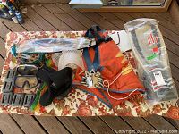 Photo of the entire scuba/snorkeling gear lot laid out on a floral patterned tablecloth. Shows orange buoyancy vest, pair of diving boots, masks, fishing spear, fins sealed in package, and mesh bag.