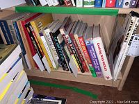 Photo of multiple cookbooks and vintage car shop books arranged on a wooden shelf, covers and titles visible.