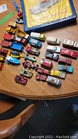 Overview of all diecast vehicles laid out on round wooden table, showing various models, colors, and a boxed set.