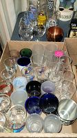 Shot glasses, tumblers, and various vintage drink glasses arranged in a box, showcasing different styles and sizes of glassware.