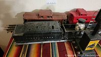 Black Lionel coal tender with red caboose and brown wooden car behind