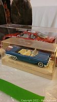 Two diecast model cars displayed in plastic cases, blue Cadillac Eldorado convertible 1953 and red Dale Earnhardt car with detailed interior