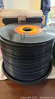 Stack of approximately 30 black vinyl 45 RPM records without sleeves, tightly packed in a case.