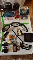 Full overview of lots with black shoes, vintage car models, shaving mug with brush, goggles, lighters, binoculars, decorative pistol brush, and round tin.