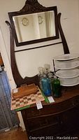 Full view of vintage wooden wash stand cabinet with large framed mirror and several items placed on top.