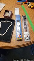 Lot overview with pearl necklace, pocket watch in box, two Disney wristwatches in packaging, on a wooden table with other items.