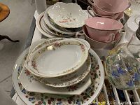 Various floral patterned ceramic plates, bowls, and cups with pink and white colors stacked on a table.