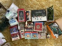 Overview of all vintage Christmas decorations including boxed mini houses, trees, figurines, snow bag, and loose pieces arranged on carpet.